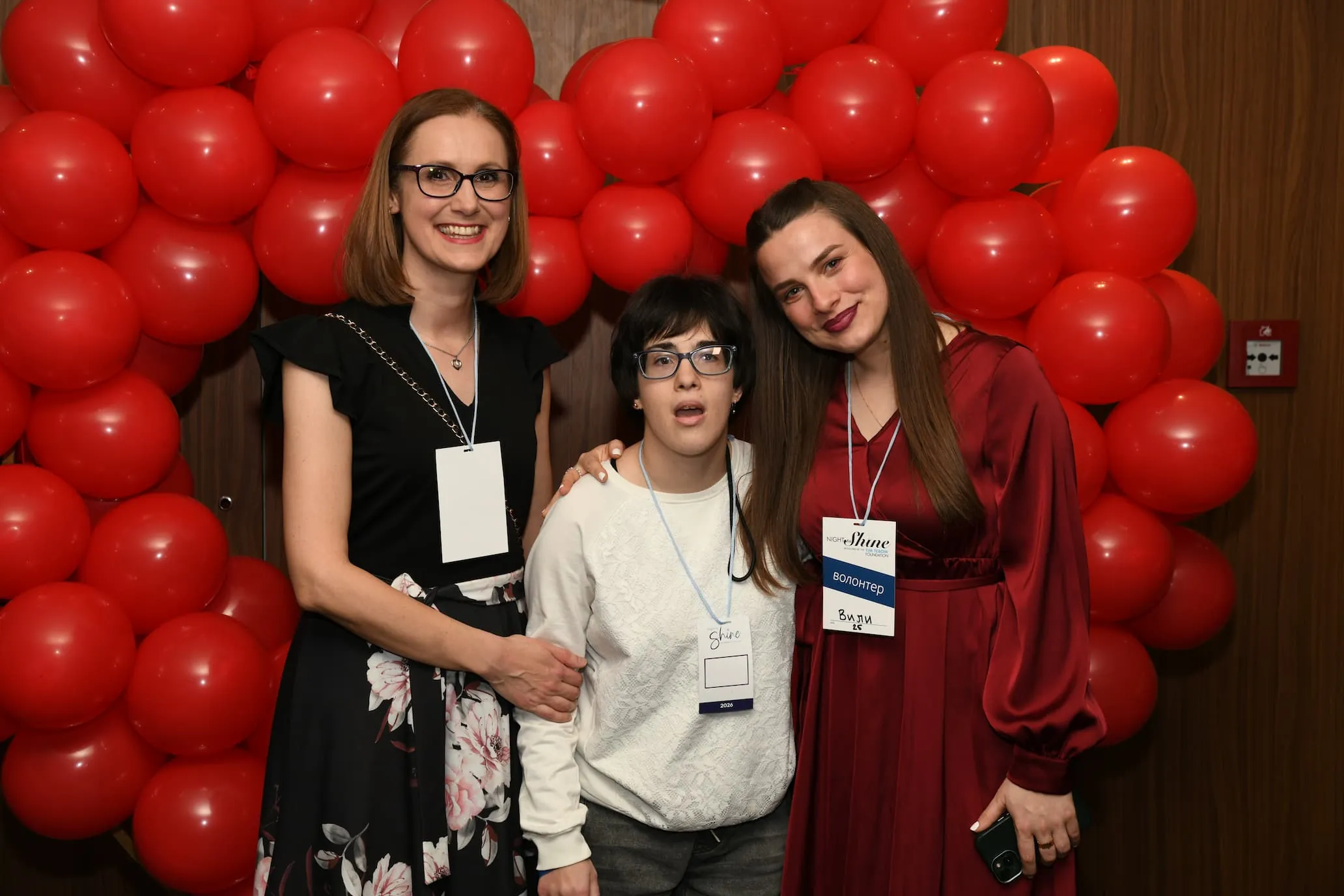 Тројца пријатели се смеат пред црвена арка од балони на Night to Shine